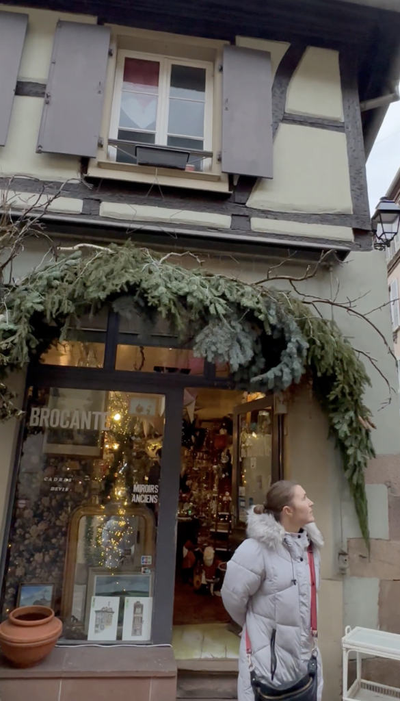 Woman standing outside a decorated shop in Colmar during the Christmas season