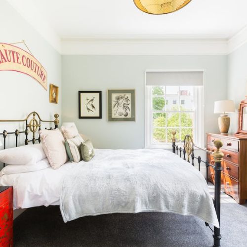 Bright bedroom in a Gloucester Airbnb with a brass bed, Haute Couture sign, and large window overlooking the park.