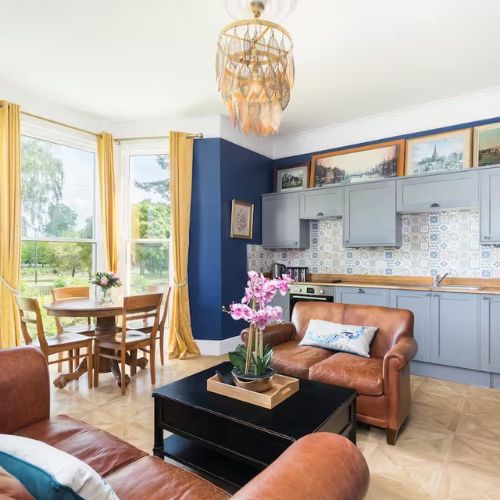 Bright living room of an Airbnb in Gloucester with blue walls, yellow curtains, and a view of the park.