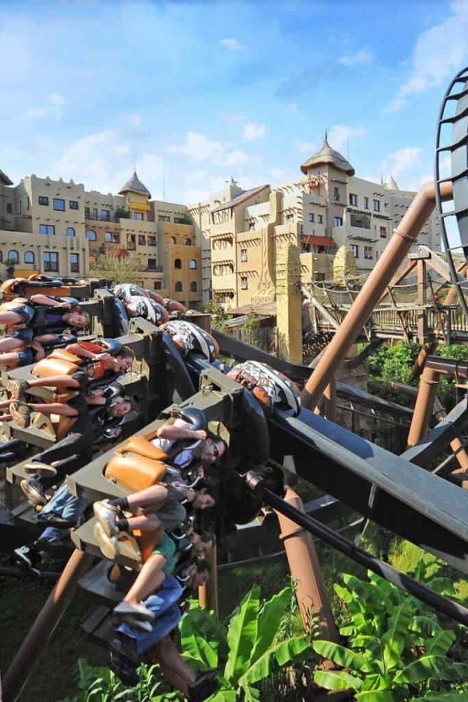 Riders on the Black Mamba inverted roller coaster at Phantasialand suspended upside down with the Africa-themed Hotel Matamba visible in the background