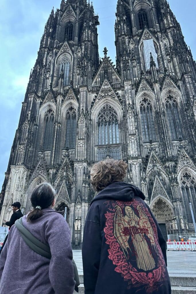Two visitors looking up at the Gothic facade of Cologne Cathedral showing the immense scale of the Kölner Dom