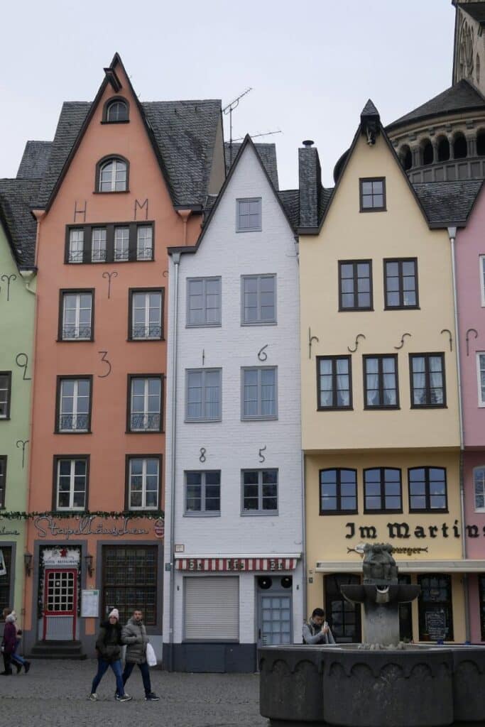 The iconic pastel-colored narrow houses of Cologne's Altstadt at Fischmarkt square with a Romanesque church visible to the right