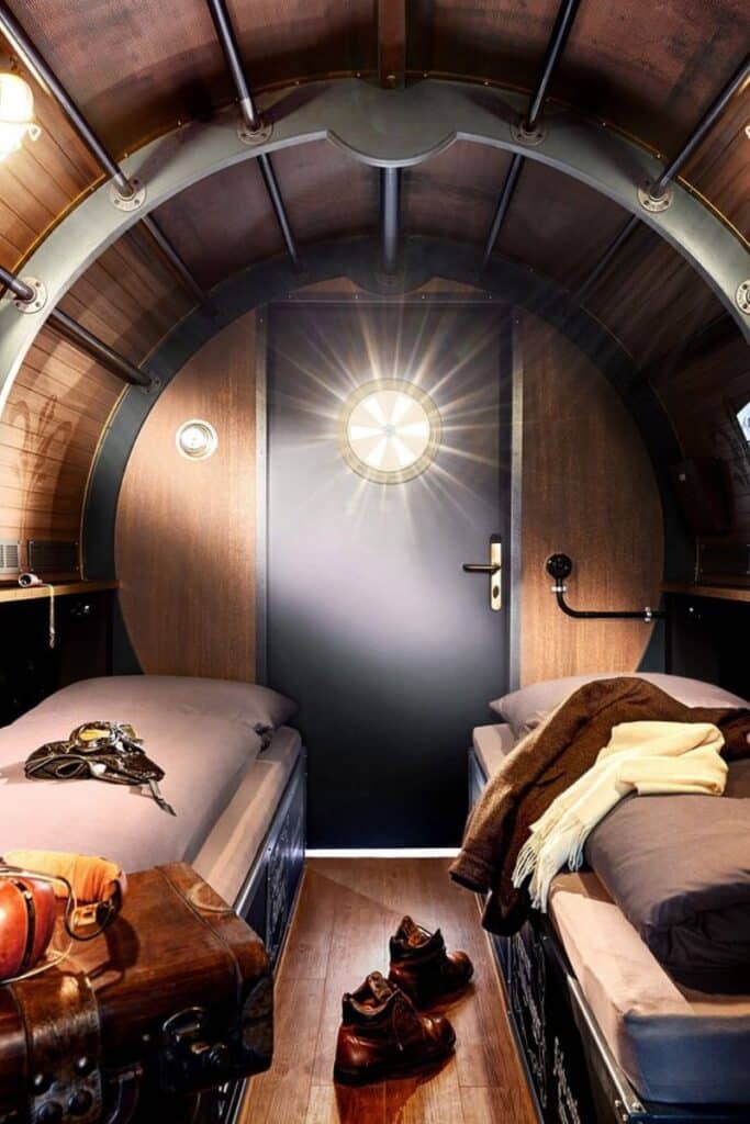 An aviation-themed room inside Hotel Charles Lindbergh at Phantasialand designed as an aircraft fuselage with curved wooden ceiling and leather-tufted walls