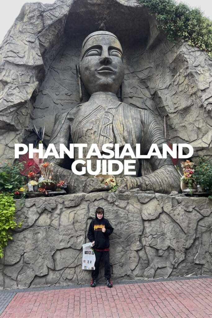 Dylan standing in front of the giant Asia-themed deity statue carved into rock at Phantasialand, with red parasols and floral offerings at its base