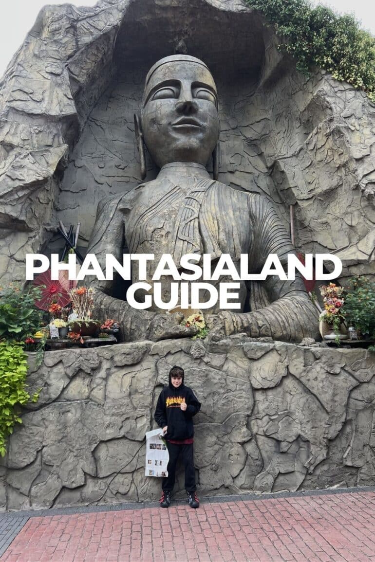Dylan standing in front of the giant Asia-themed deity statue carved into rock at Phantasialand, with red parasols and floral offerings at its base