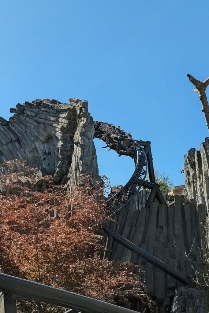 Taron roller coaster train cresting a rise through the dramatic basalt rock formations of Klugheim at Phantasialand with autumn red foliage below