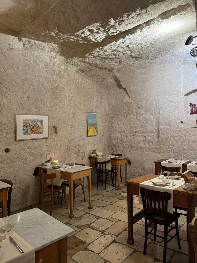 Stone cave dining room with marble tables and vaulted tuff ceiling inside a restaurant in the Sassi di Matera