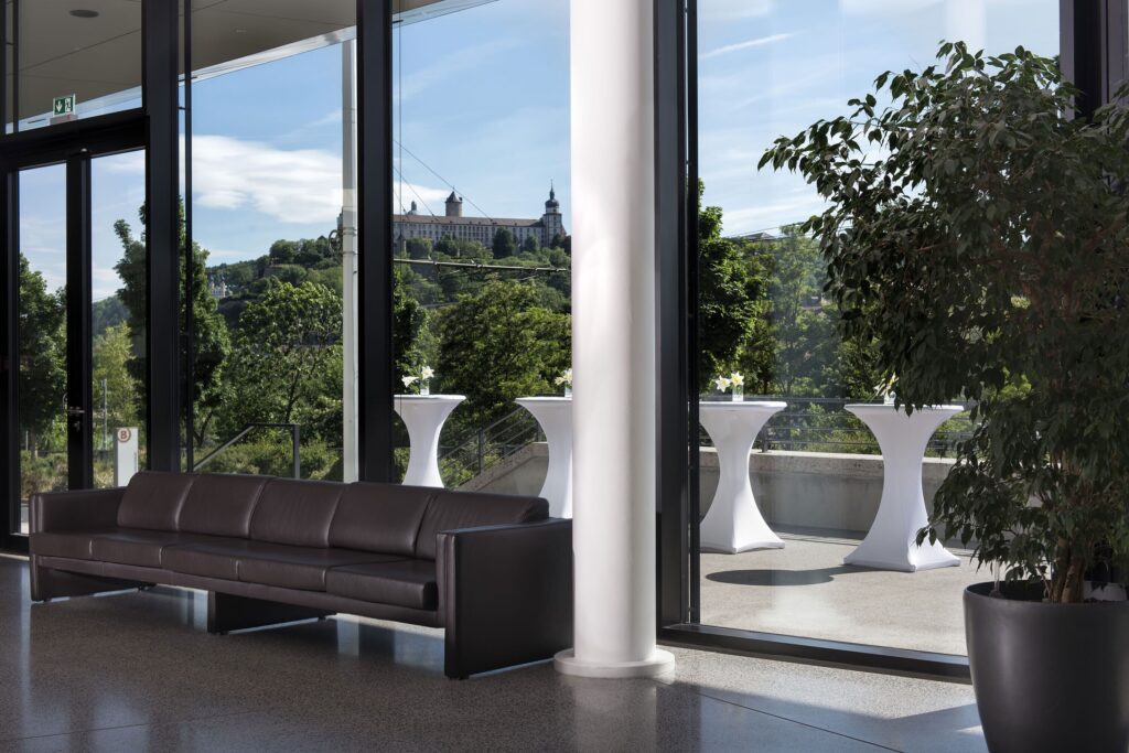 Lobby seating at the Melchior Park Hotel in Würzburg, with a view of Marienberg Fortress through floor-to-ceiling windows.