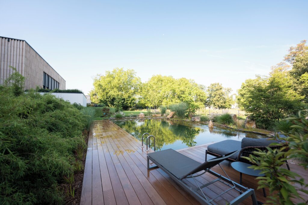 The natural outdoor swimming pond at the Melchior Park Hotel in Würzburg, with a wooden deck and lounge chair.