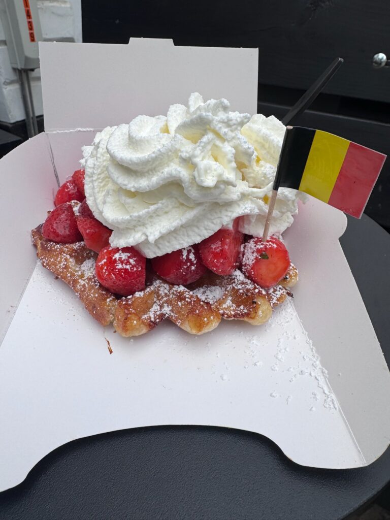 Belgian waffle topped with fresh strawberries and whipped cream, served with a small Belgian flag in Antwerp.