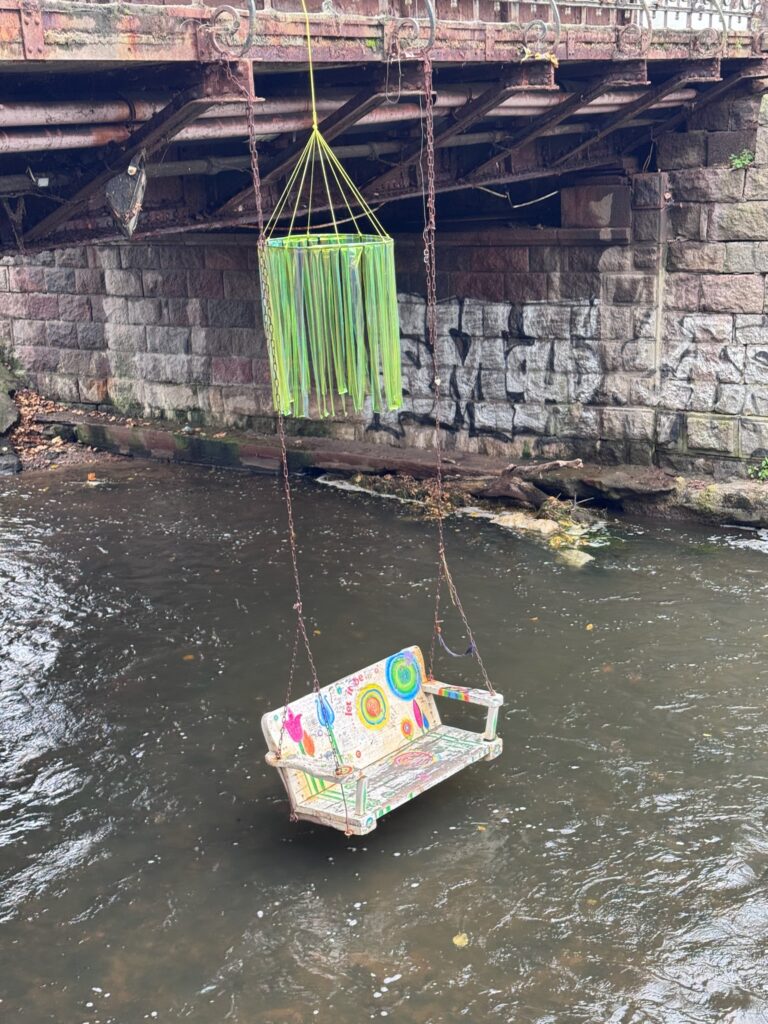 Colorful suspended bench hanging above the Vilnelė River beneath a bridge in the Užupis neighborhood