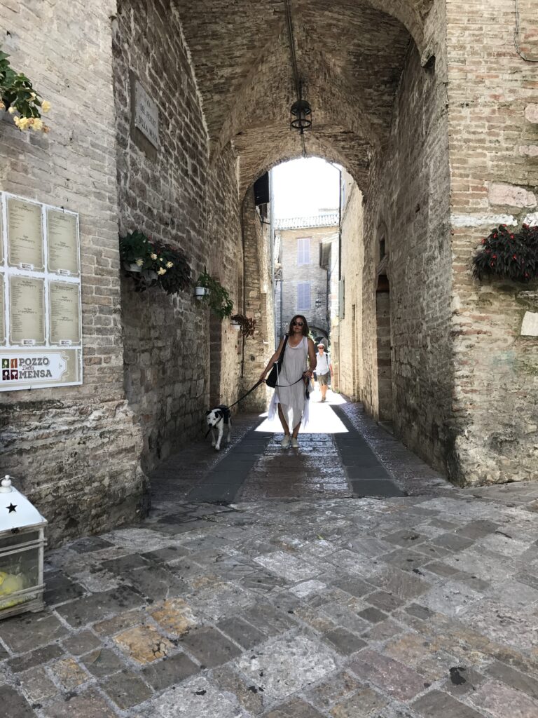 Stone archway in Assisi with a woman walking a dog through the historic center