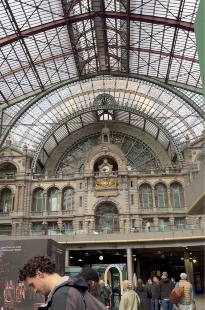 Ornate stone facade and clock beneath the arched glass and iron roof inside Antwerp Central Station in Belgium.