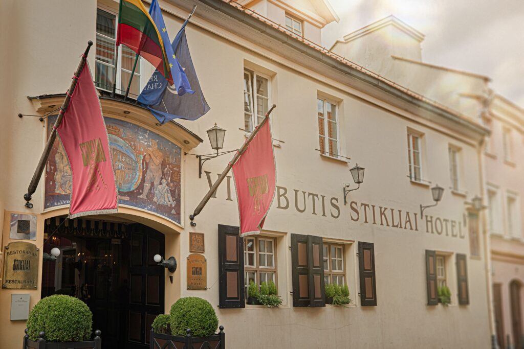 Exterior entrance of Stikliai Hotel in Vilnius Old Town with historic architecture, decorative flags and potted greenery.