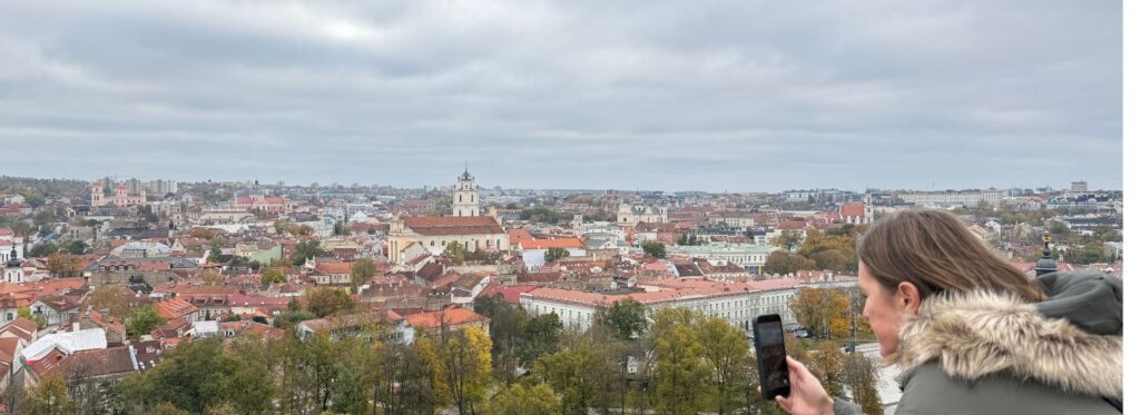 View over Vilnius Old Town in autumn, with historic churches, red rooftops and a visitor overlooking the city.