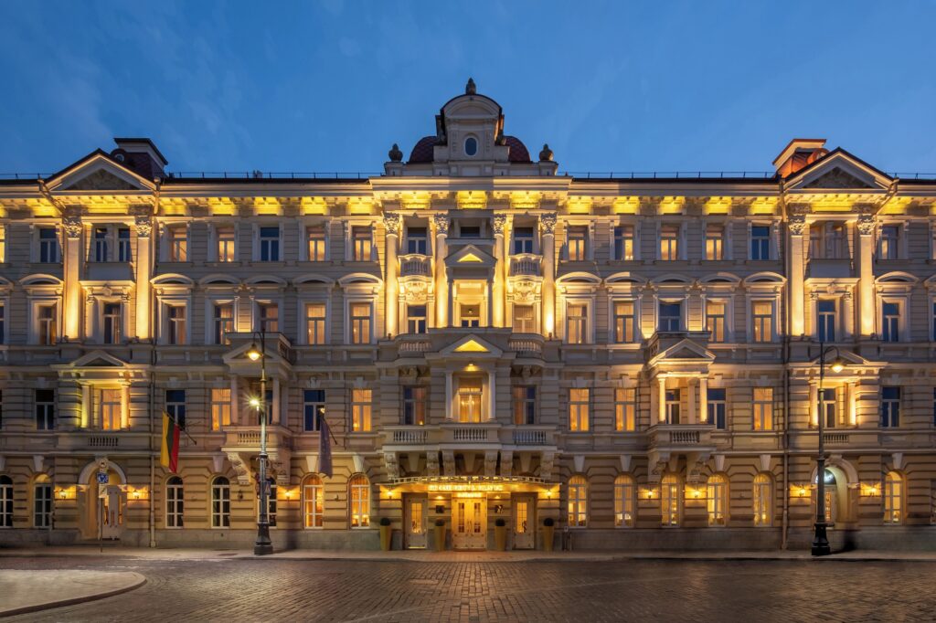 Illuminated exterior of Grand Hotel Vilnius, Curio Collection by Hilton, at dusk near Cathedral Square in Vilnius Old Town.