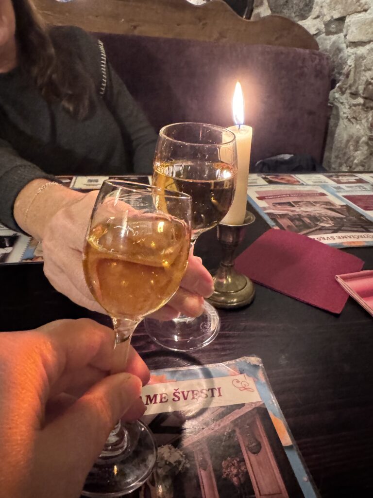 Two glasses of white wine raised in a toast by candlelight at Bernelių Užeiga in Vilnius