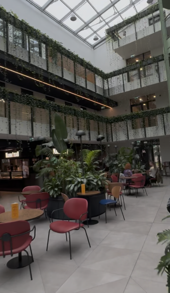 Glass-roofed atrium with hanging plants and red chairs at Paupys Market food hall in Vilnius